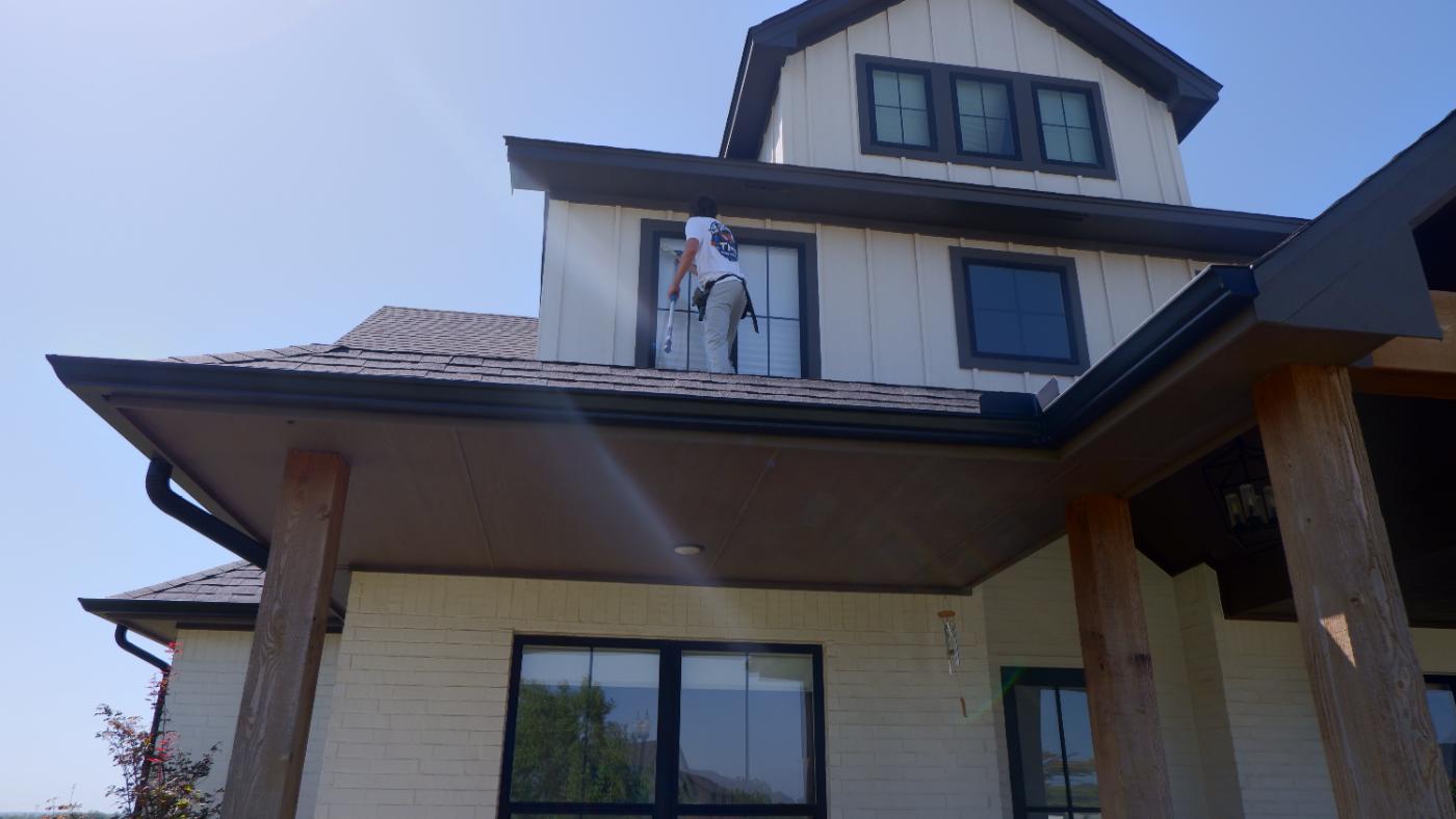 TMI crew member cleaning a second-story window from the roofline
